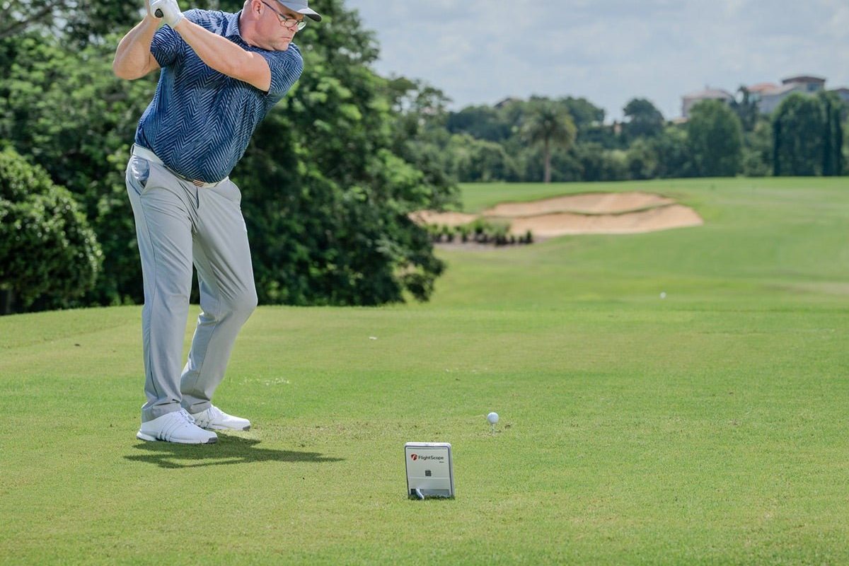 Portable golf simulator setup: a golfer hitting outdoors with a FlightScope Mevo Gen2 launch monitor set up behind the ball